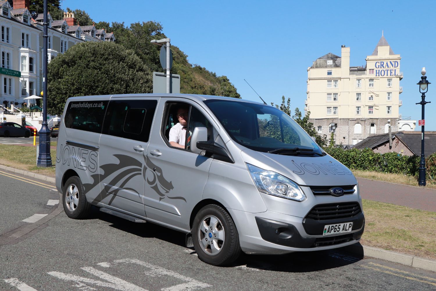 The Ford Tourneos used for the door to door element of the Jones Holiday experience carry a silver version of the corporate livery. This example is seen at Llandudno Pier with one of Alpine Travel’s current driver trainees at the wheel